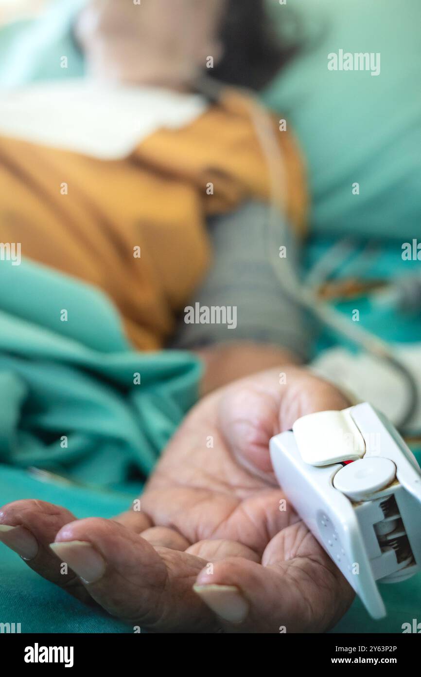 Ricoverato malato donna anziana asiatica in trattamento come paziente ricoverato sdraiato nel ossimetro del letto sul pollice per la misurazione della saturazione, del polso e della frequenza cardiaca Foto Stock