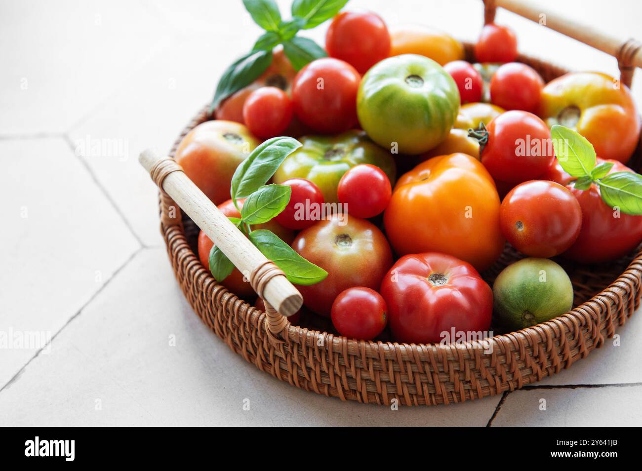 Un'abbondante collezione di pomodori colorati riempie un cesto intrecciato, caratterizzato da varie dimensioni e sfumature che si appoggiano su un ripiano della cucina a fine estate Foto Stock
