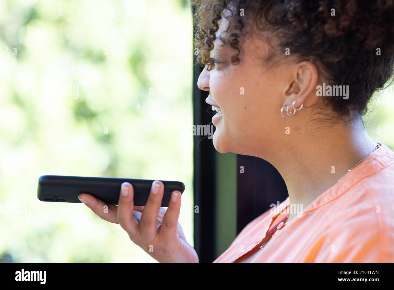 Parla nello smartphone, la donna sorride mentre comunica con l'assistente vocale, a casa Foto Stock