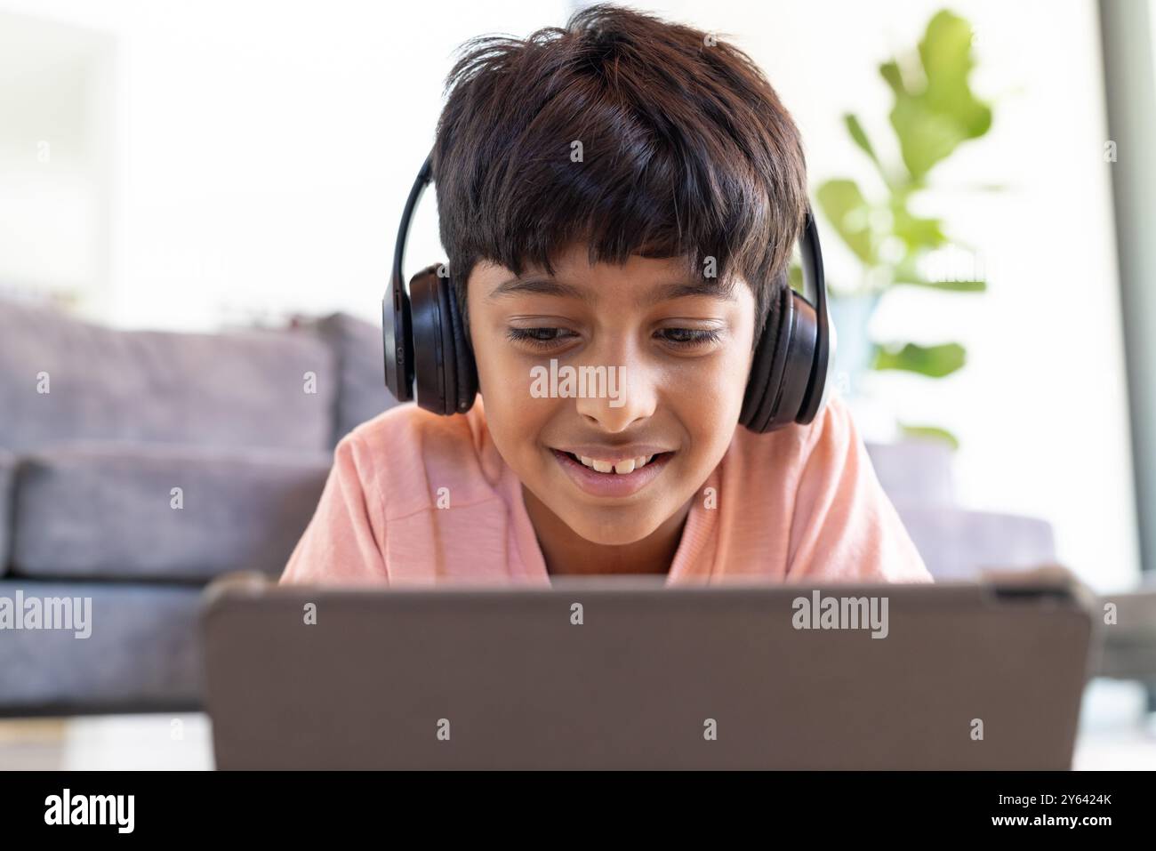 Indossa le cuffie, un ragazzo indiano sorridente e guarda lo schermo del tablet a casa Foto Stock