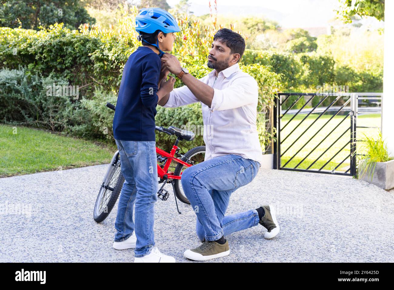 Aiutando il figlio con il casco, padre indiano che prepara il bambino per un giro in bicicletta all'aperto Foto Stock