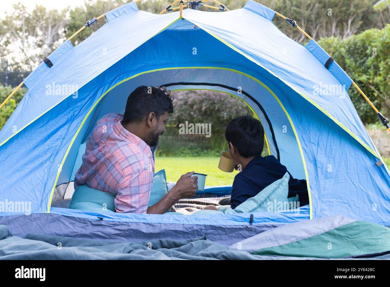 Campeggio in tenda, padre e figlio indiani che si godono bevande calde all'aperto Foto Stock