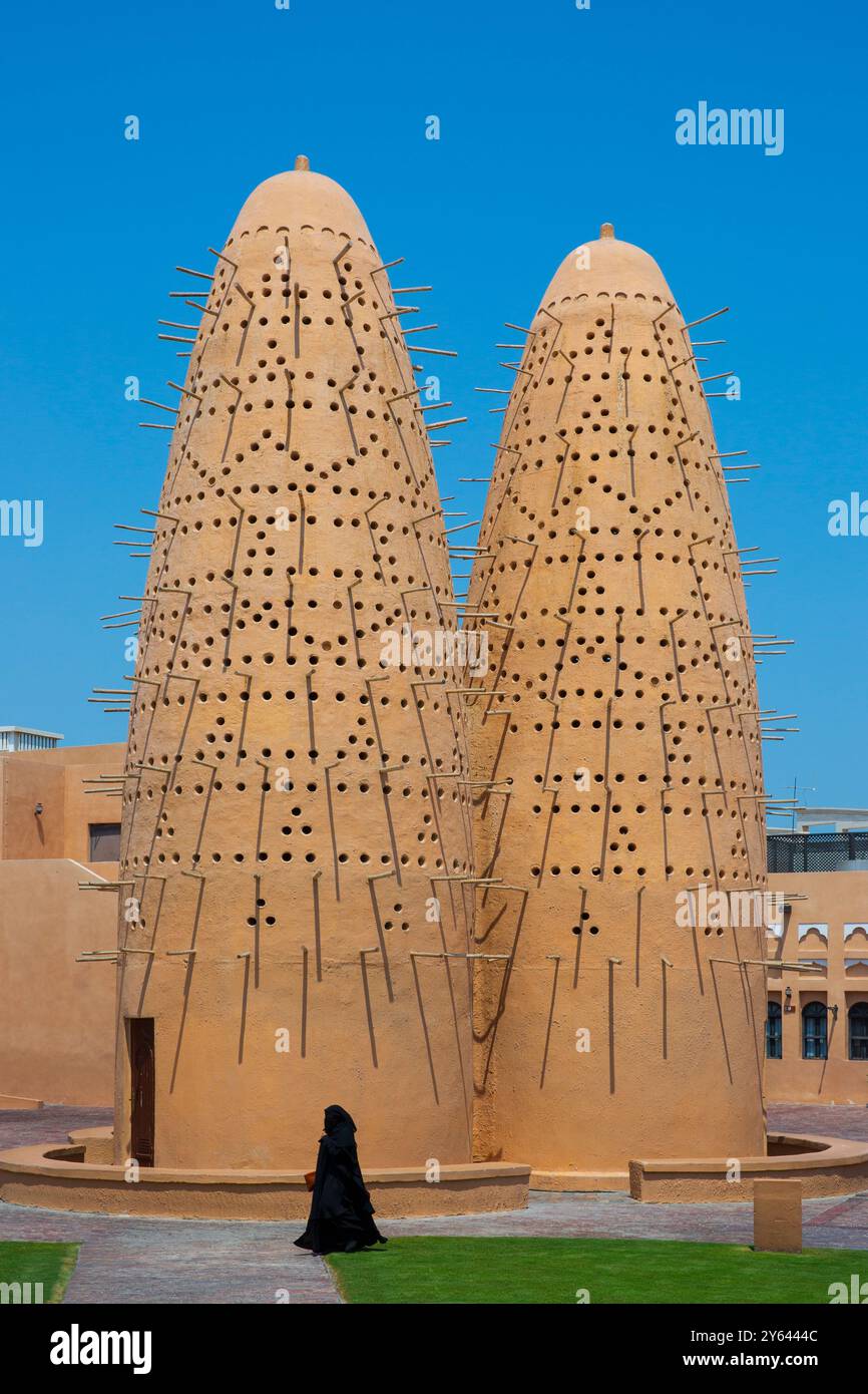 Una donna in tradizionale chador nero (indumento) che passa davanti alle torri dei piccioni del Villaggio culturale Katara a Doha, Qatar Foto Stock