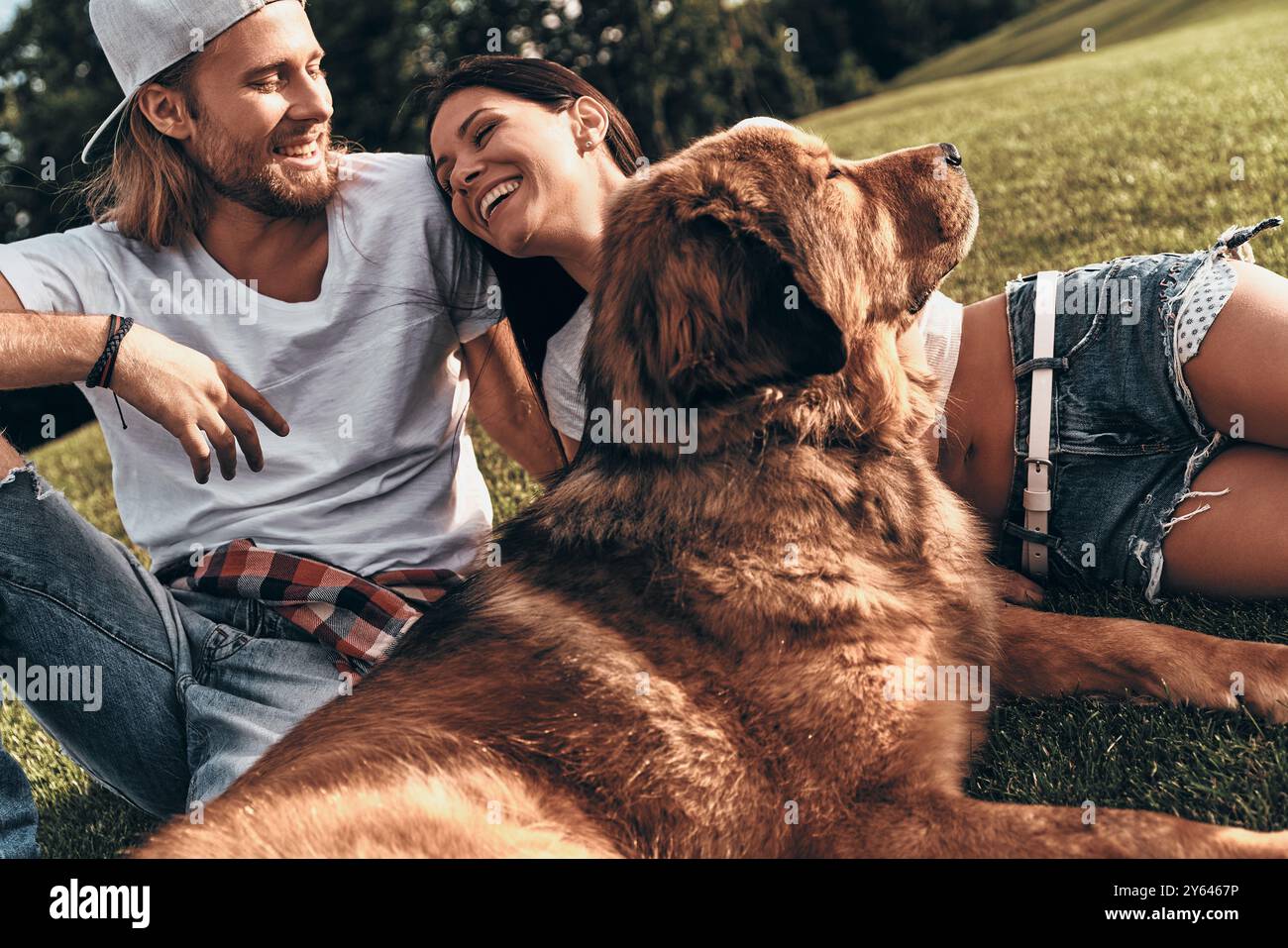 Nient'altro che amore. Giovane coppia moderna sdraiata sull'erba con il proprio cane mentre trascorre del tempo libero nel parco Foto Stock