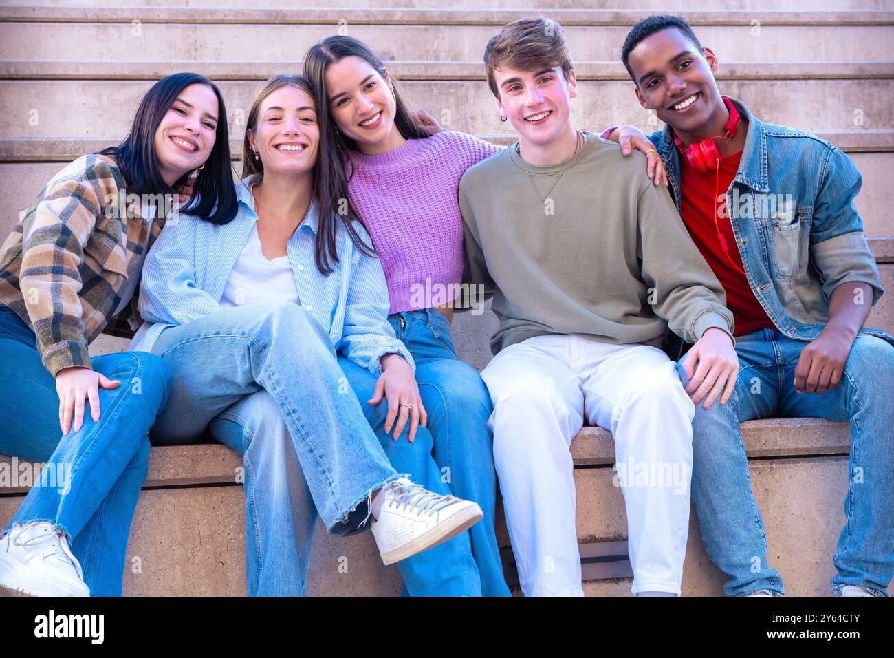 Adolescenti sorridenti seduti sulle scale che si abbracciano guardando la macchina fotografica Foto Stock