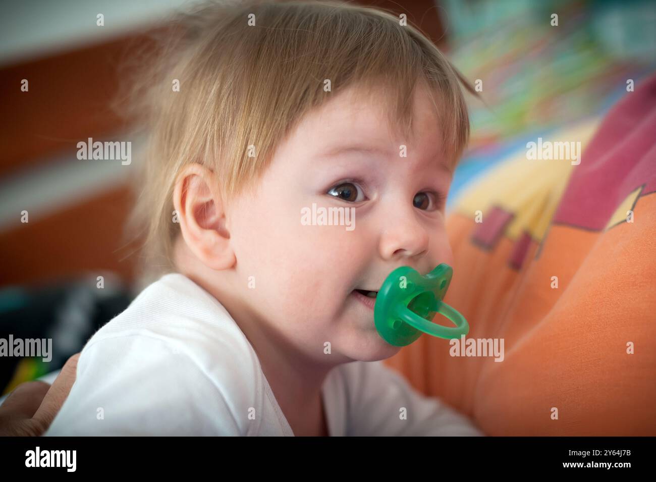 Un adorabile bambino con i capelli ruvidi e un succhietto esplora i loro vivaci dintorni, mostrando uno spirito gioioso e una curiosità giocosa. Foto Stock