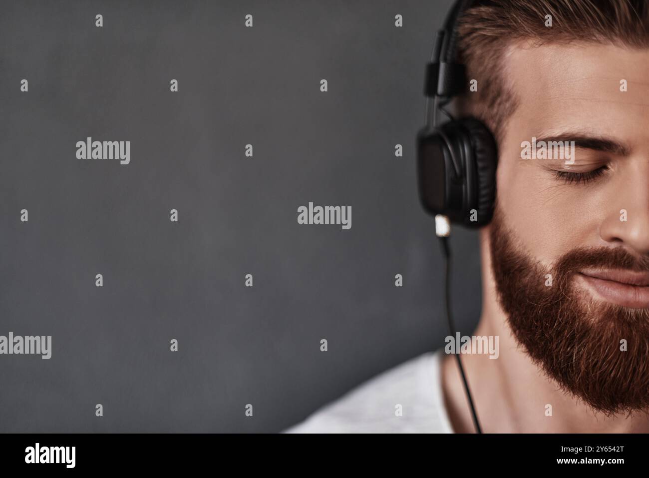 Ascoltando con il cuore. Primo piano di un giovane uomo dall'aspetto accattivante, metà faccia che ascolta la musica stando in piedi su uno sfondo grigio Foto Stock