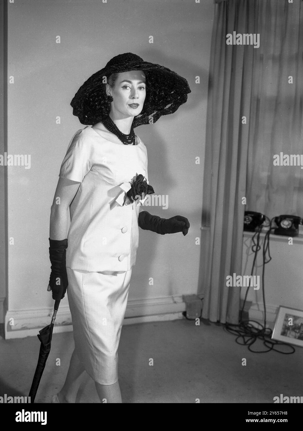 Pat o'Reilly indossa una tunica pomeridiana di seta beige con una rosa nera durante una mostra della collezione Christian Dior - London per l'estate 1959. Anche il grande cappello di paglia e i guanti sono neri . 4 marzo 1959 Foto Stock