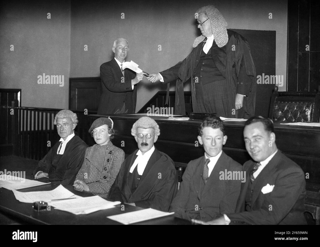 Una cerimonia pittoresca che risale a molti secoli fa ha avuto luogo presso il tribunale quando il Re Remembrancer Sir George Bonner ha ricevuto gli affitti annuali di cessazione - sei scarpe da cavallo e 61 unghie sono state consegnate solennemente per conto degli sceriffi di Middlesex per aver affittato il sito di una vecchia fucina che si trovava nello Strand mentre la Ciry Corporation si era offerta un'ascia con un gancio per banconote e due mazzi di ramoscelli al posto dei rubinetti per un'antica proprietà nello Shropshire - la foto mostra Sir George Bonner che riceve l'ascia di guerra dal rappresentante della City Corporation alla cerimonia del 25 ottobre 1934 Foto Stock