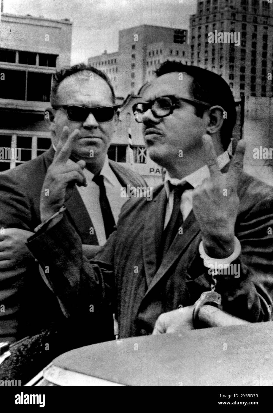 Bosch ha condotto via il leader cubano in esilio, il dottor Orlando Bosch, dà un segno di vittoria ai fotografi e grida ' Vittoria per la liberazione cubana ', mentre è guidato da un maresciallo americano (a sinistra) in una macchina d'attesa dopo il suo arresto. Il dottor Bosch e altri otto esuli cubani che sono stati arrestati sono accusati di aver sparato un fucile privo di rinculo contro la nave polacca Polancia, mentre era in porto l'11 ottobre 1968 Foto Stock