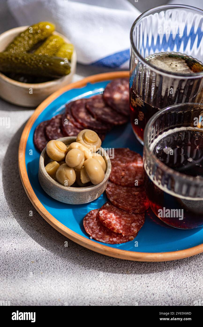 Un pasto tradizionale con kvass, due tipi di salsicce, funghi fermentati e un lato di cetriolo, servito splendidamente su un vivace piatto blu Foto Stock