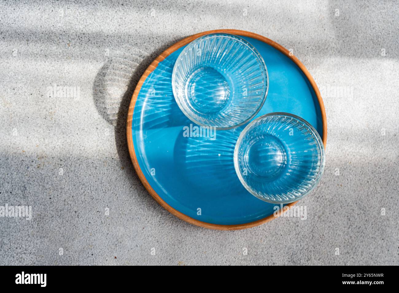 Un'immagine artistica che mostra due ciotole di vetro blu trasparente disposte all'interno di una grande ciotola blu, tutte disposte su una superficie sabbiosa Foto Stock