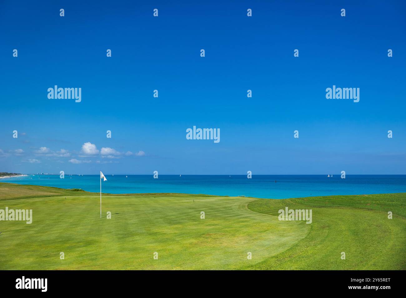 Un tranquillo campo da golf a Cuba, caratterizzato da verdi immacolati con uno sfondo mozzafiato del turchese Mar dei Caraibi e delle barche a vela. Foto Stock