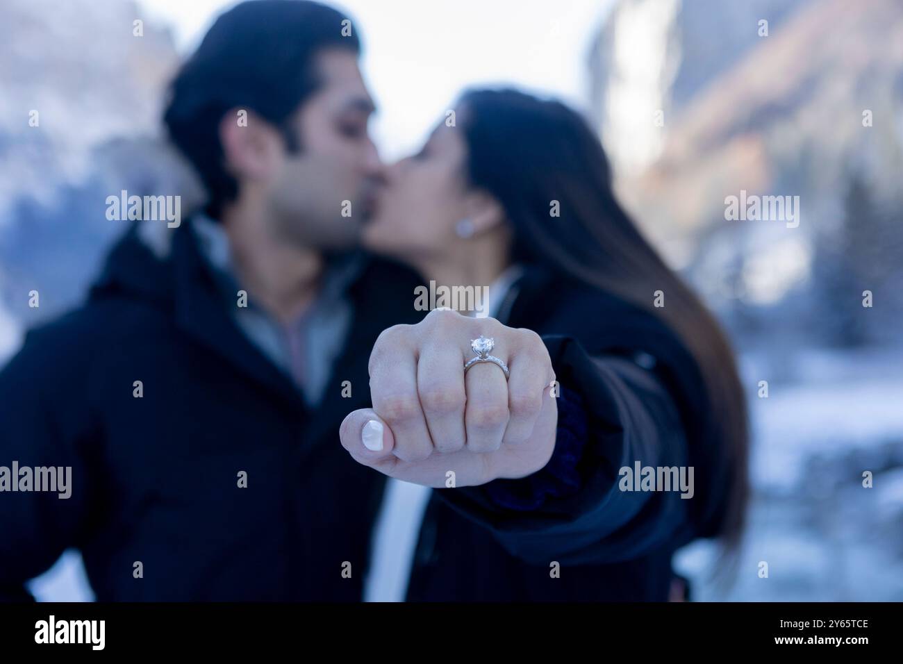 Una coppia indiana condivide un bacio in un ambiente invernale, celebrando il loro fidanzamento. La donna sta mostrando in modo prominente il suo anello di fidanzamento al cameriere Foto Stock