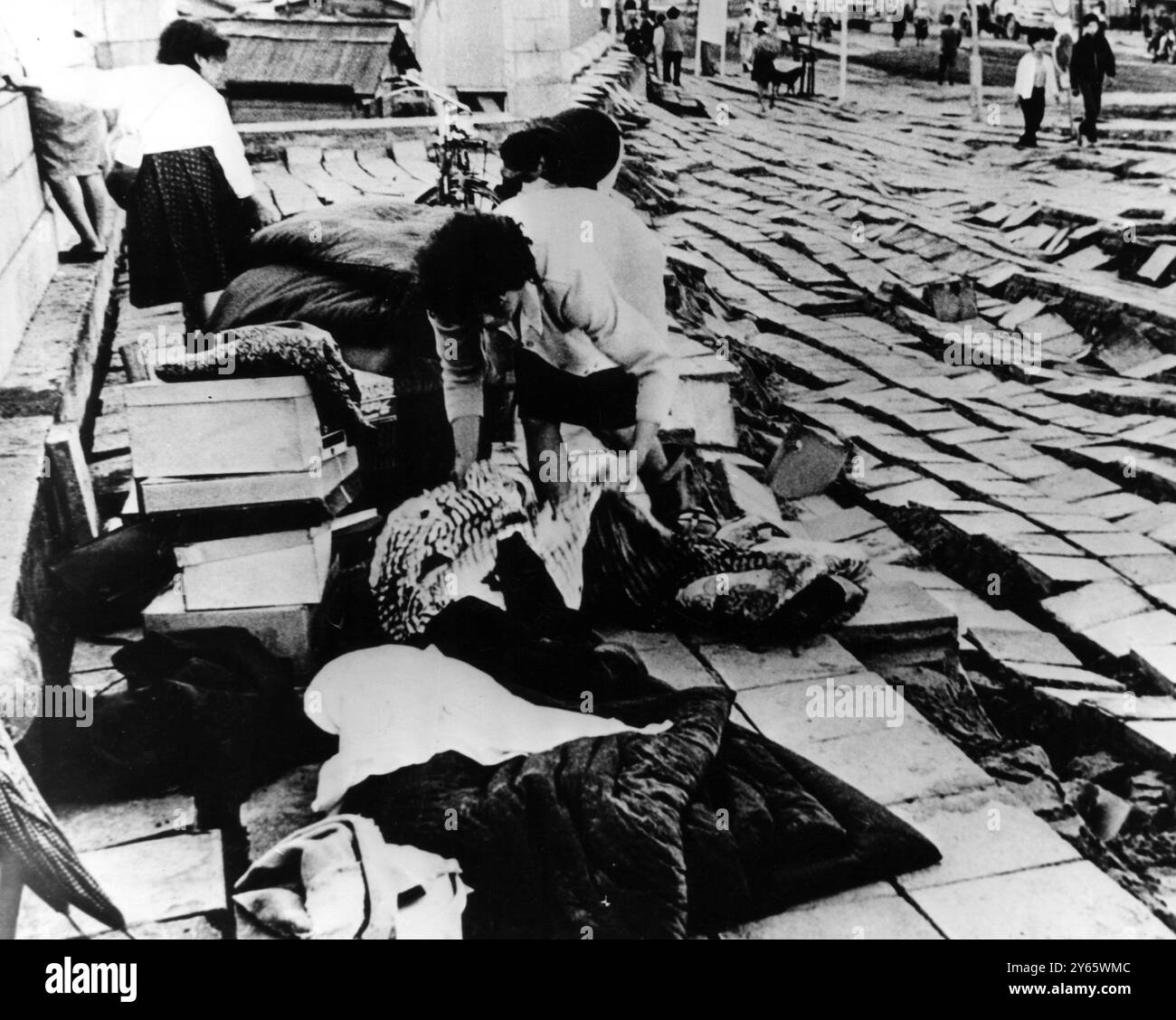 I senzatetto sismico riuniscono fasci di effetti personali sul margine relativamente piano di una strada ora dislivellata , come un tappeto di cuore incasinato. Giugno 1964 Foto Stock