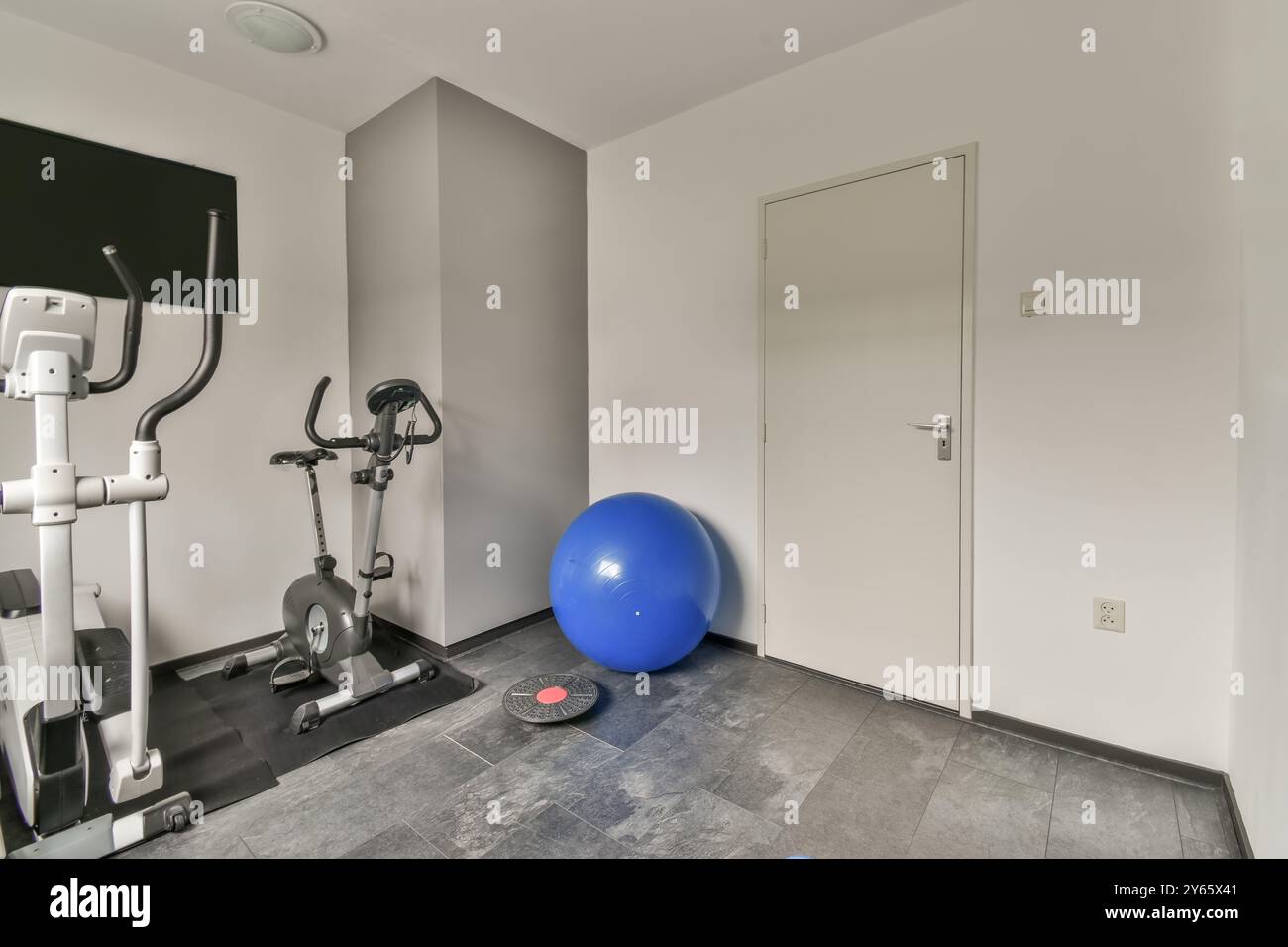 Uno spazio per la palestra domestico compatto e moderno con cyclette, macchina ellittica e pallone da allenamento per l'equilibrio. Foto Stock