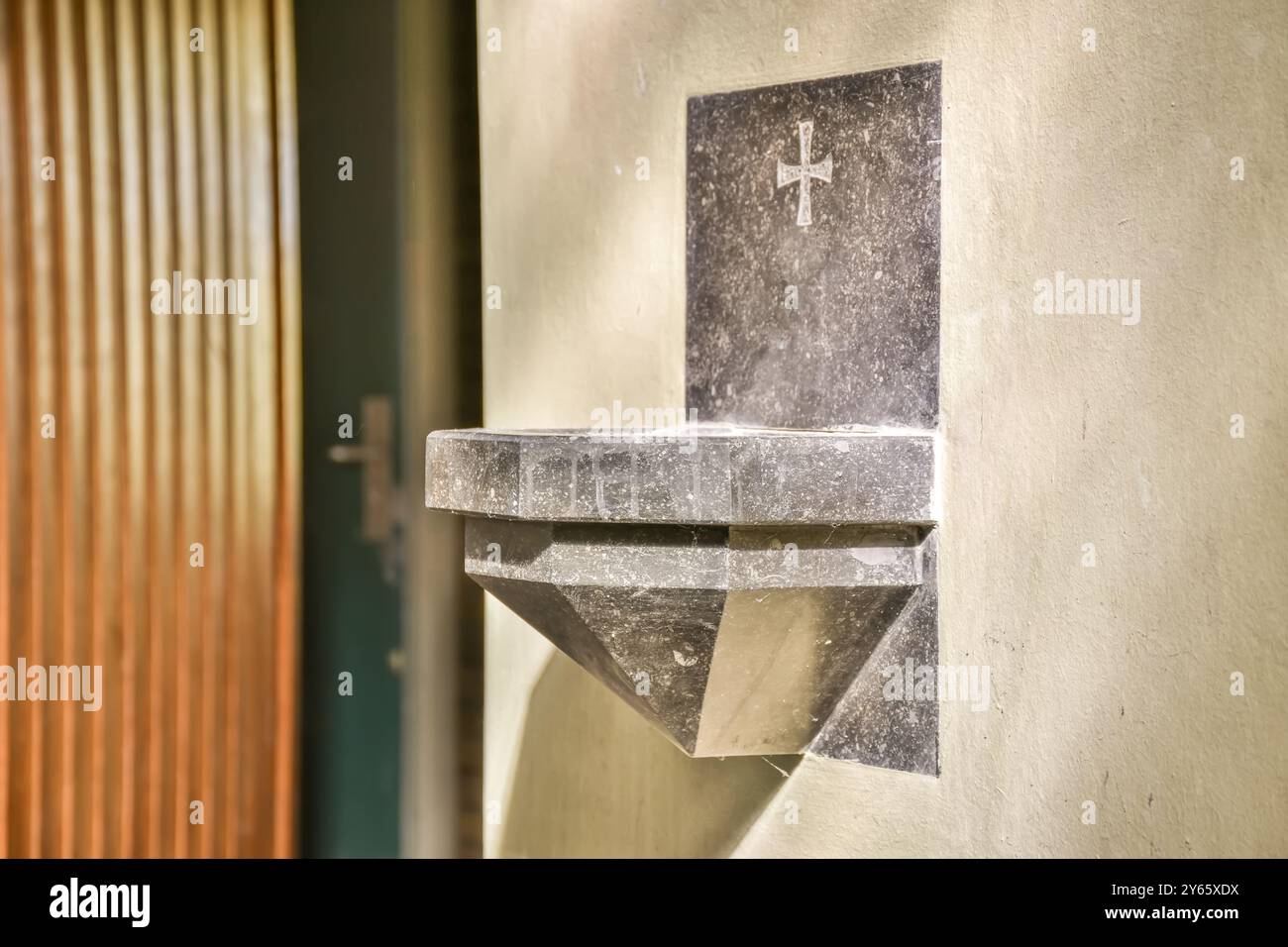 Primo piano di una fonte d'acqua sacra in marmo, fissata su una parete della chiesa, con una semplice incisione a croce. Foto Stock
