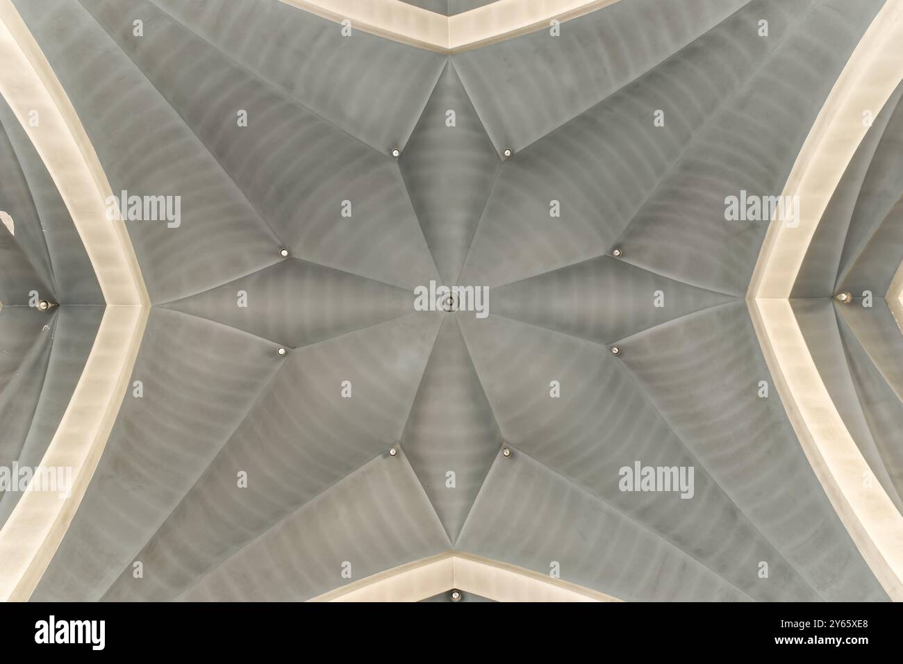 Questa immagine cattura l'intricato motivo simmetrico di una moderna struttura a soffitto con illuminazione soffusa. Foto Stock