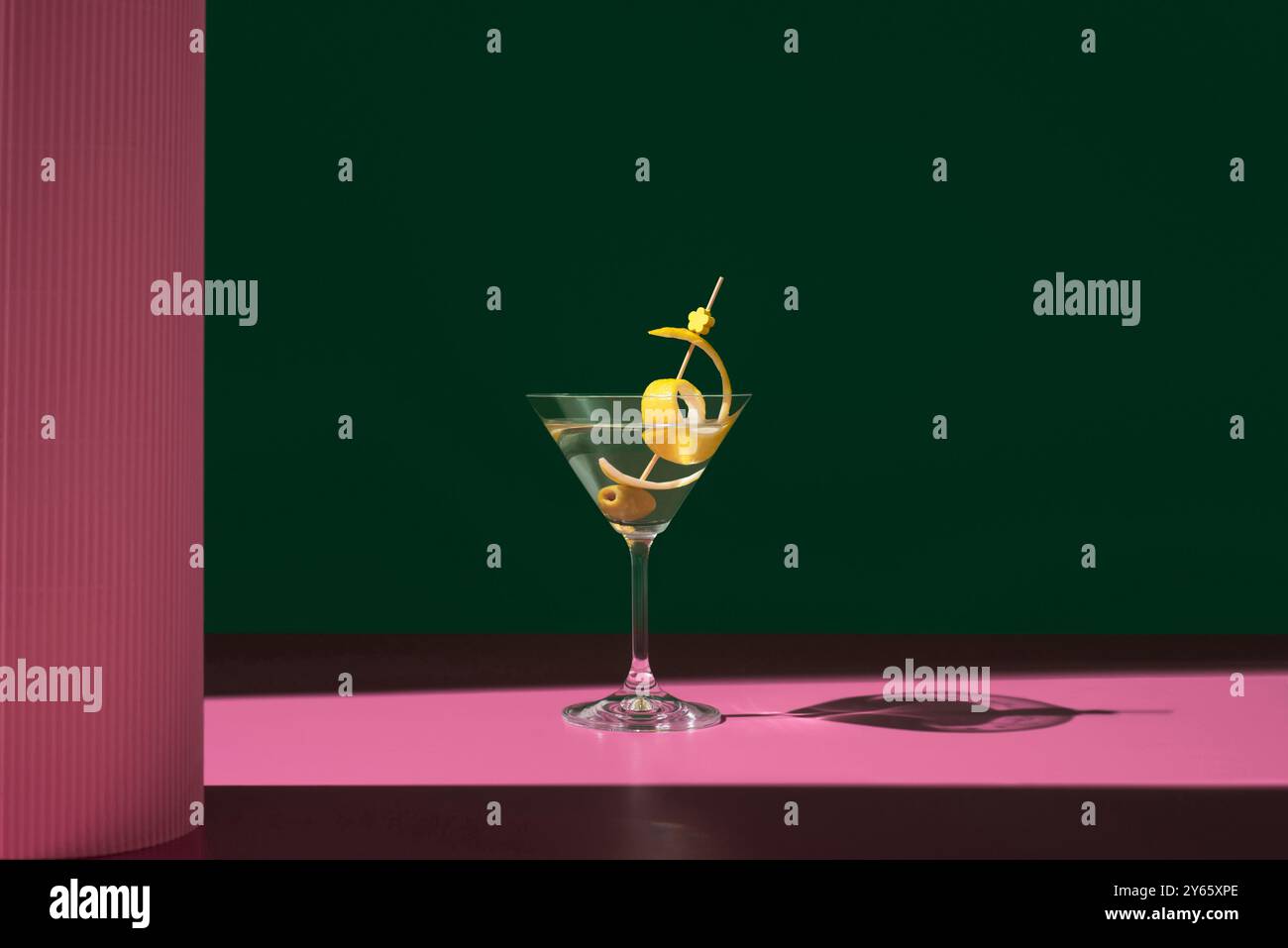Un classico cocktail Martini secco, guarnito con olive verdi e un ricciolo di scorza di limone, elegantemente presentato su uno sfondo rosa e verde Foto Stock