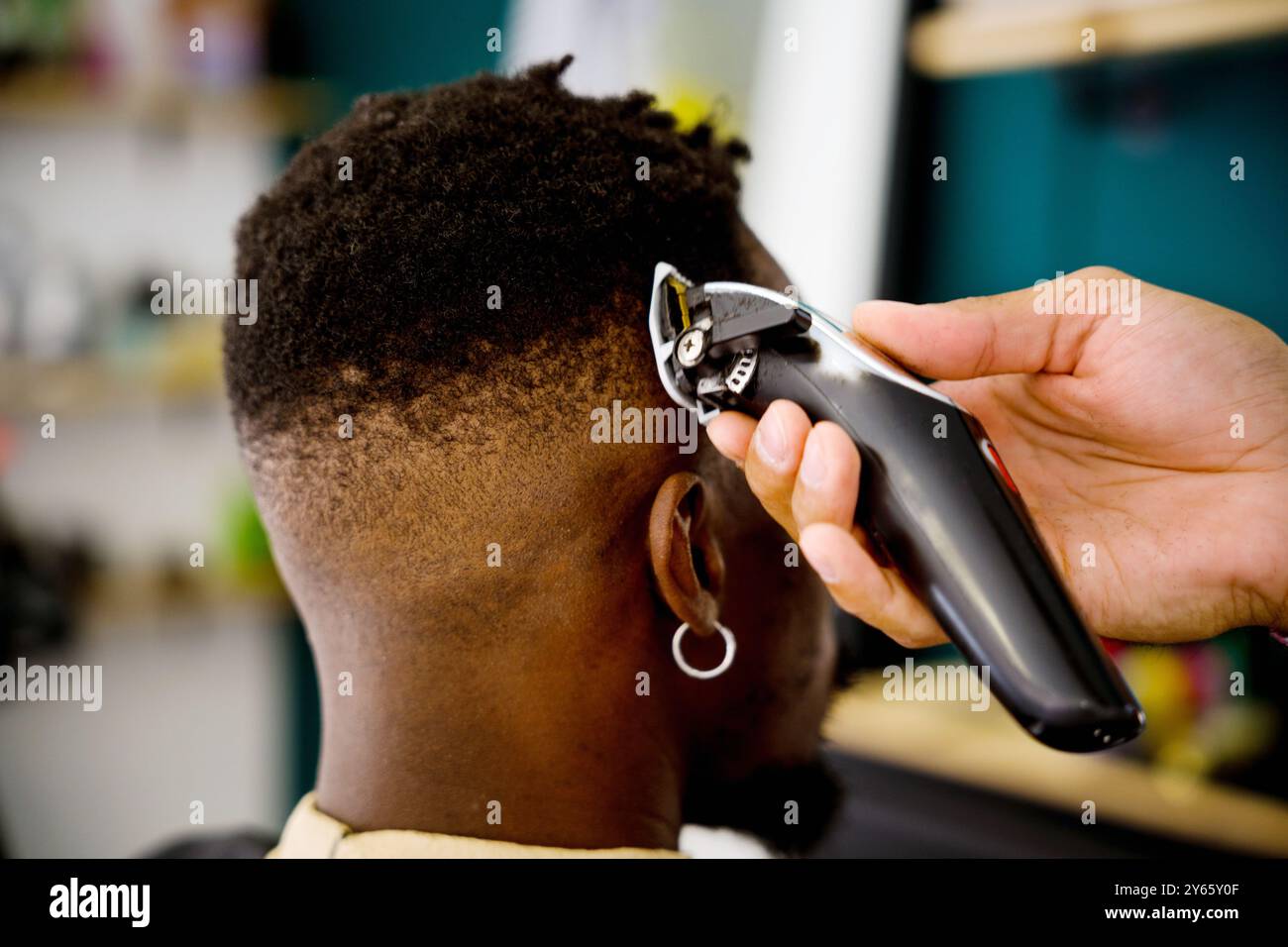 Immagine ravvicinata di un barbiere professionista, che utilizza i regolacapelli elettrici per modellare i capelli di un uomo nero in un barbiere a tema costiero Foto Stock