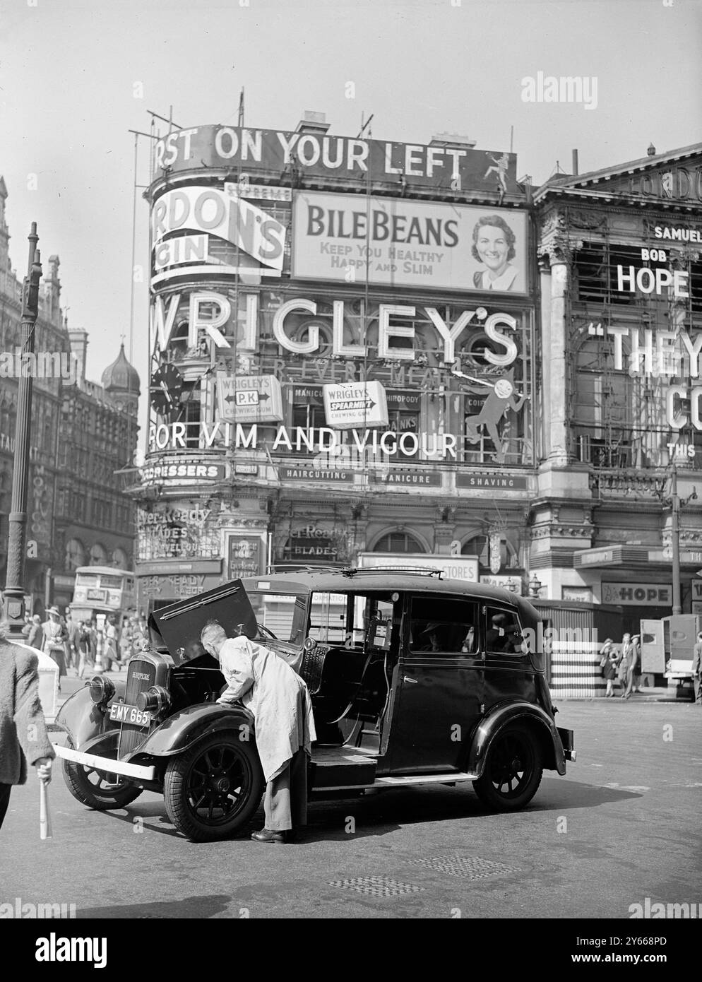 Piccadilly Circus. c.1943MAN che si occupa della sua auto in avaria con pubblicità sullo sfondo, tra cui Bile Beans e chewing gum di Wrigley Foto Stock