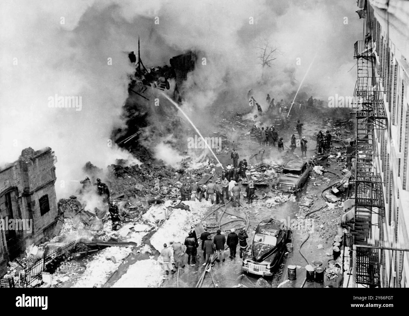 A seguito del disastro del doppio aereo di New York oggi, queste fiamme a Brooklyn, dove la United Airliner è atterrata, continuano a diffondersi negli edifici che sembrano essere stati colpiti da una bomba. I vigili del fuoco continuano a combattere il fuoco e in basso a sinistra sono vicino alle rovine della chiesa metodista "pilastro del fuoco". La sezione principale dell'aereo di linea si è schiantata contro i tetti delle nostre case annesse e la grande sezione della coda è caduta sulla strada in cima a una Ford Sedan. Nove corpi gravemente bruciati sono stati rimossi da un edificio. Non si è potuto sapere immediatamente se erano passeggeri o Foto Stock