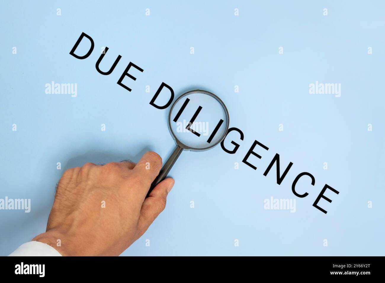 Una mano con una lente d'ingrandimento sopra le parole "DUE DILIGENCE" su sfondo blu. Business, finanza, legge, concetto di ricerca. Foto Stock