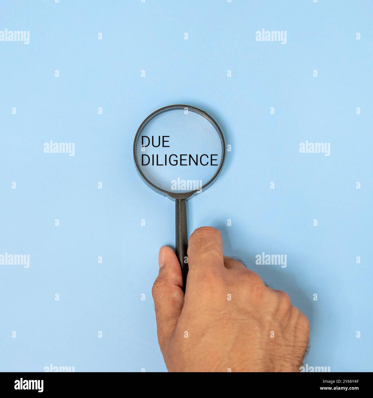 Una mano con una lente d'ingrandimento sopra le parole "DUE DILIGENCE" su sfondo blu. Business, finanza, legge, concetto di ricerca. Foto Stock