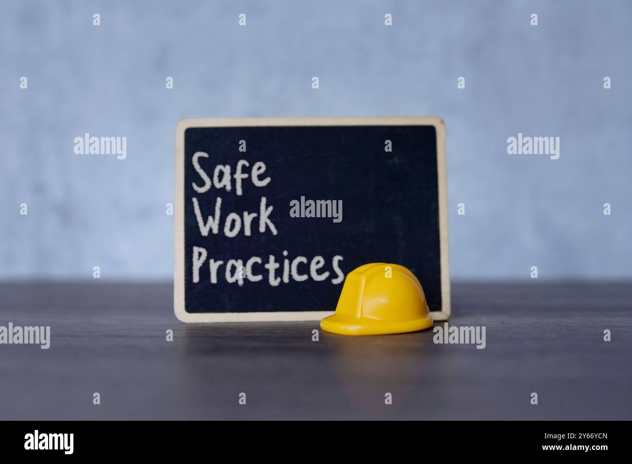 Piccola lavagna con il testo "pratiche di lavoro sicure" e elmetto giallo. Concetti di sicurezza, precauzione e standard sul luogo di lavoro. Foto Stock