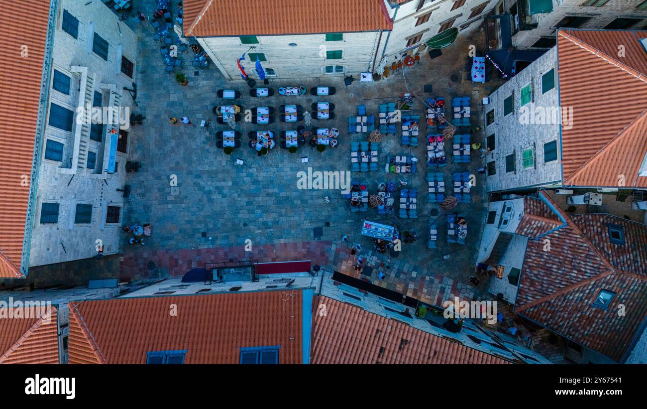 Una vivace piazza di Cattaro si anima mentre la gente del posto e i visitatori si riuniscono intorno a tavoli colorati, godendosi l'atmosfera. L'affascinante architettura e i tetti di tegole rosse fanno da cornice a questa vivace scena. Foto Stock