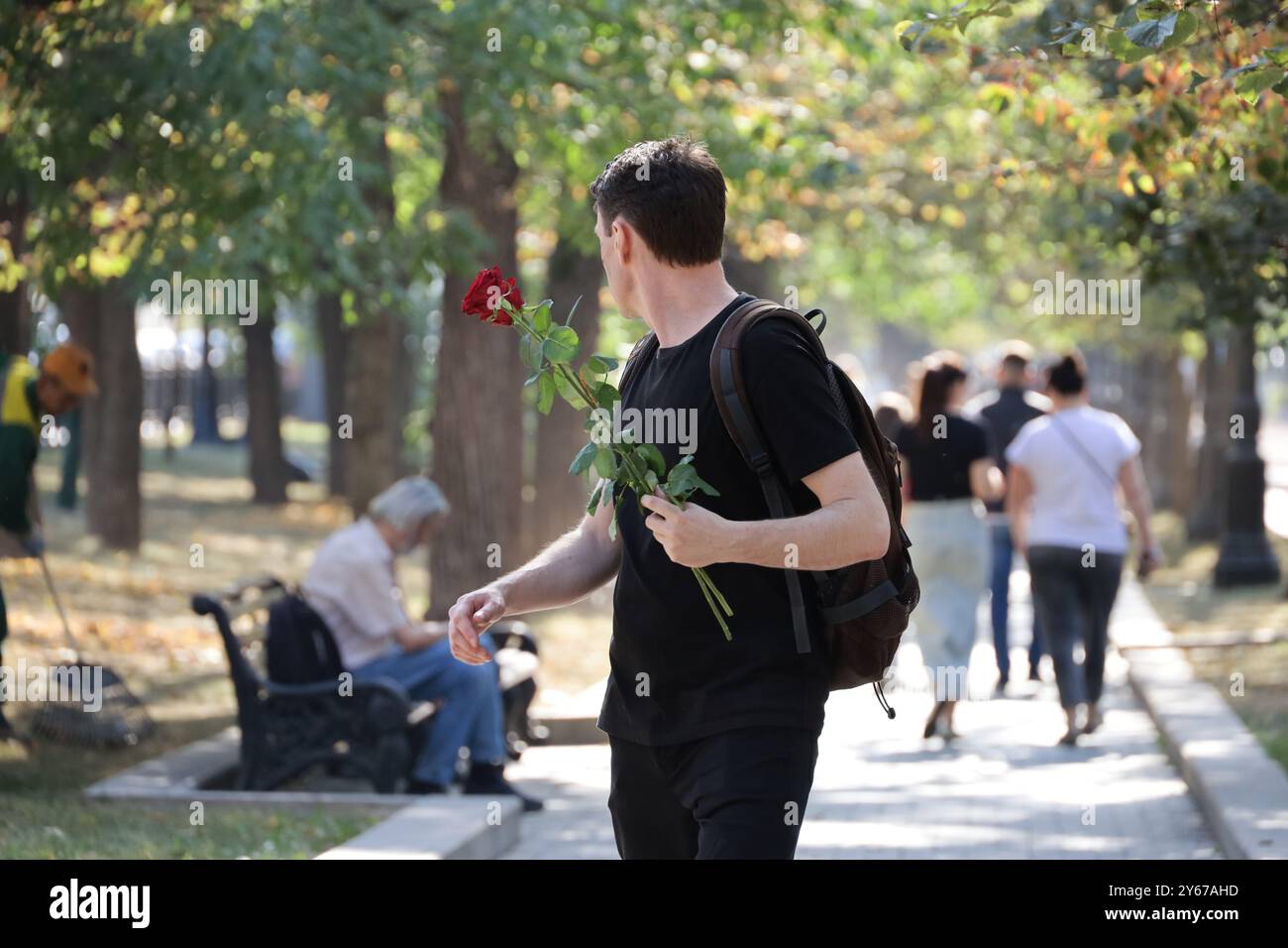 Uomo con fiori di rosa che cammina su una strada sullo sfondo della gente. Appuntamento nella città autunnale Foto Stock