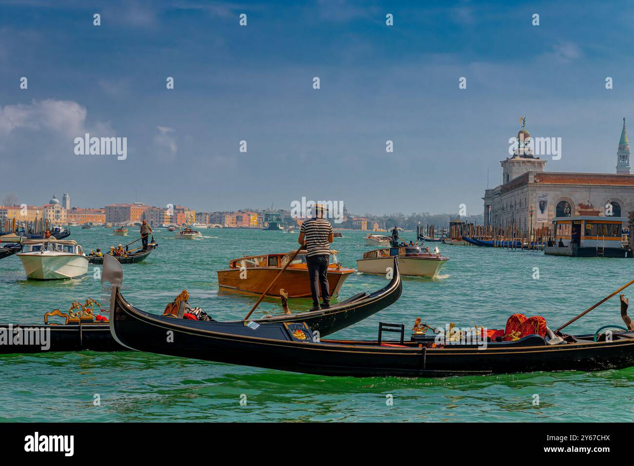 Un gondoliere e la sua gondola e taxi d'acqua privati in pieno traffico fluviale all'ingresso del Canal grande a Venezia, Italia Foto Stock