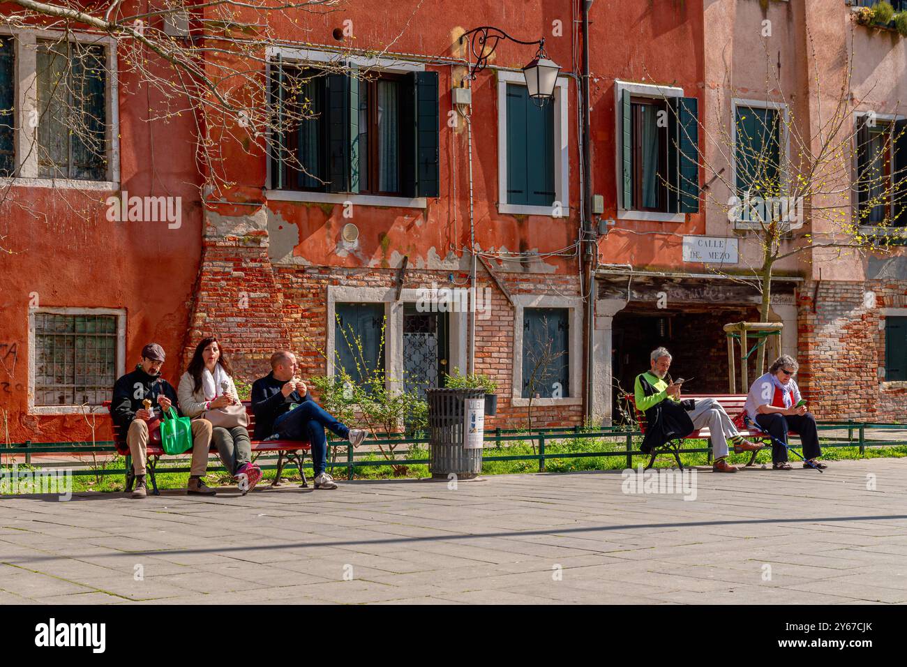 Le persone sedute sulle panchine godono del sole primaverile in campo San Giacomo, una piazza nel sestiere di Santa Croce a Venezia Foto Stock