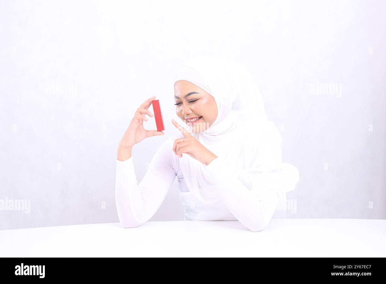 Paesaggio del trucco labbra bella giovane ragazza del velo asia sguardo allegro al rossetto mano tenendo e toccando il contenitore del rossetto isolato su sfondo bianco. Foto Stock