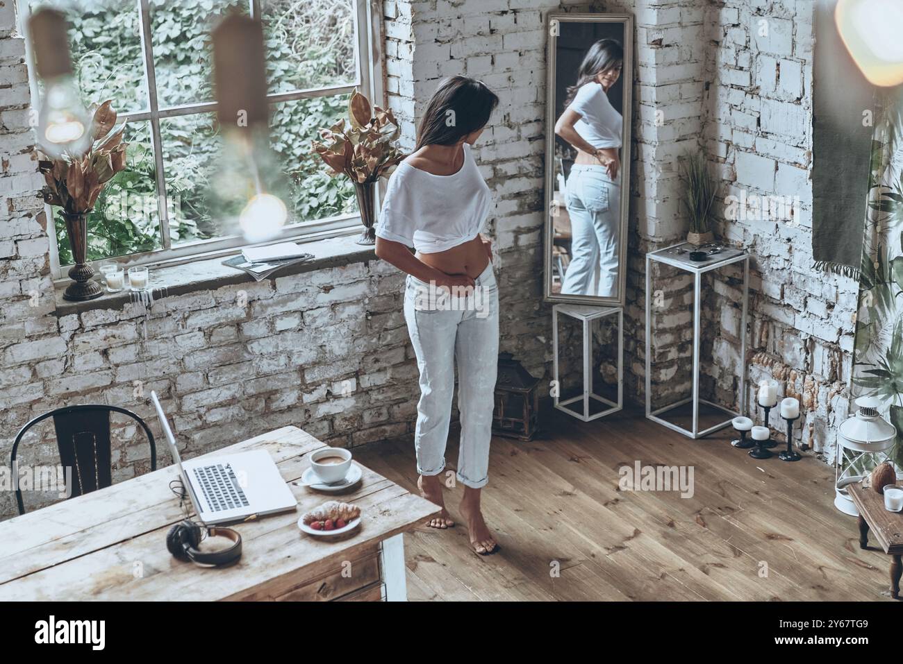 Si adatta a jeans skinny. Una giovane donna attraente che guarda allo specchio mentre indossa i jeans Foto Stock