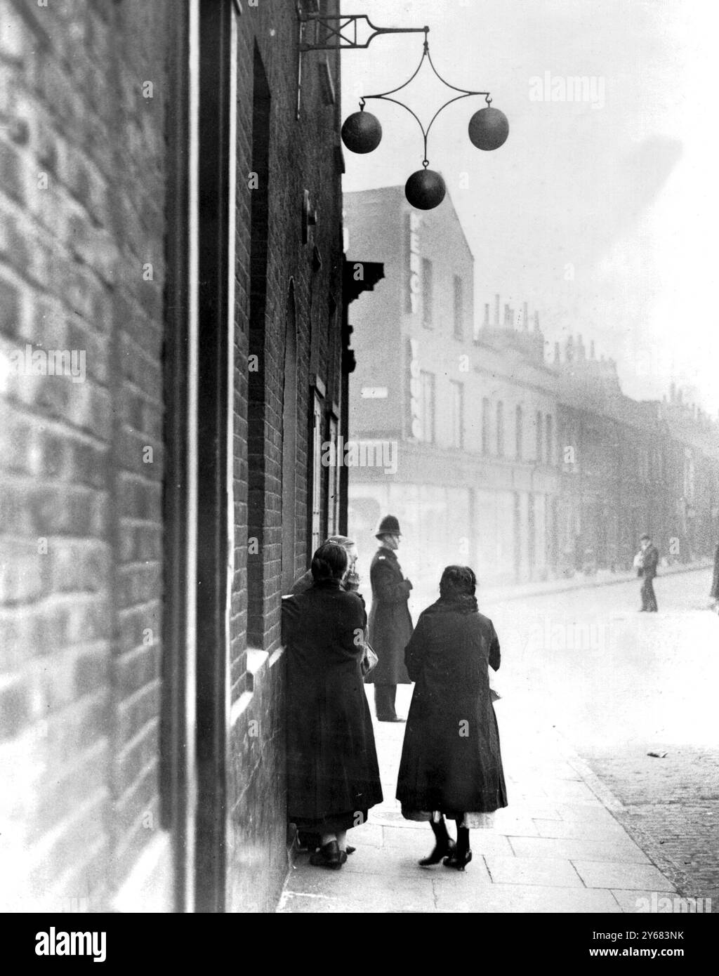 Lunedì mattina in un banco dei pegni nell'East End di Londra. Le donne aspettarono l'apertura del banco dei pegni; tutto il loro denaro era stato speso il sabato e i fasci di vestiti erano stati messi in pegno il lunedì per essere riscattati alla fine della settimana se il denaro era stato permesso. In un sondaggio è stato scoperto che una famiglia su tre utilizzava un pewnbroker. Fotografia degli anni '1930 di John Topham Foto Stock