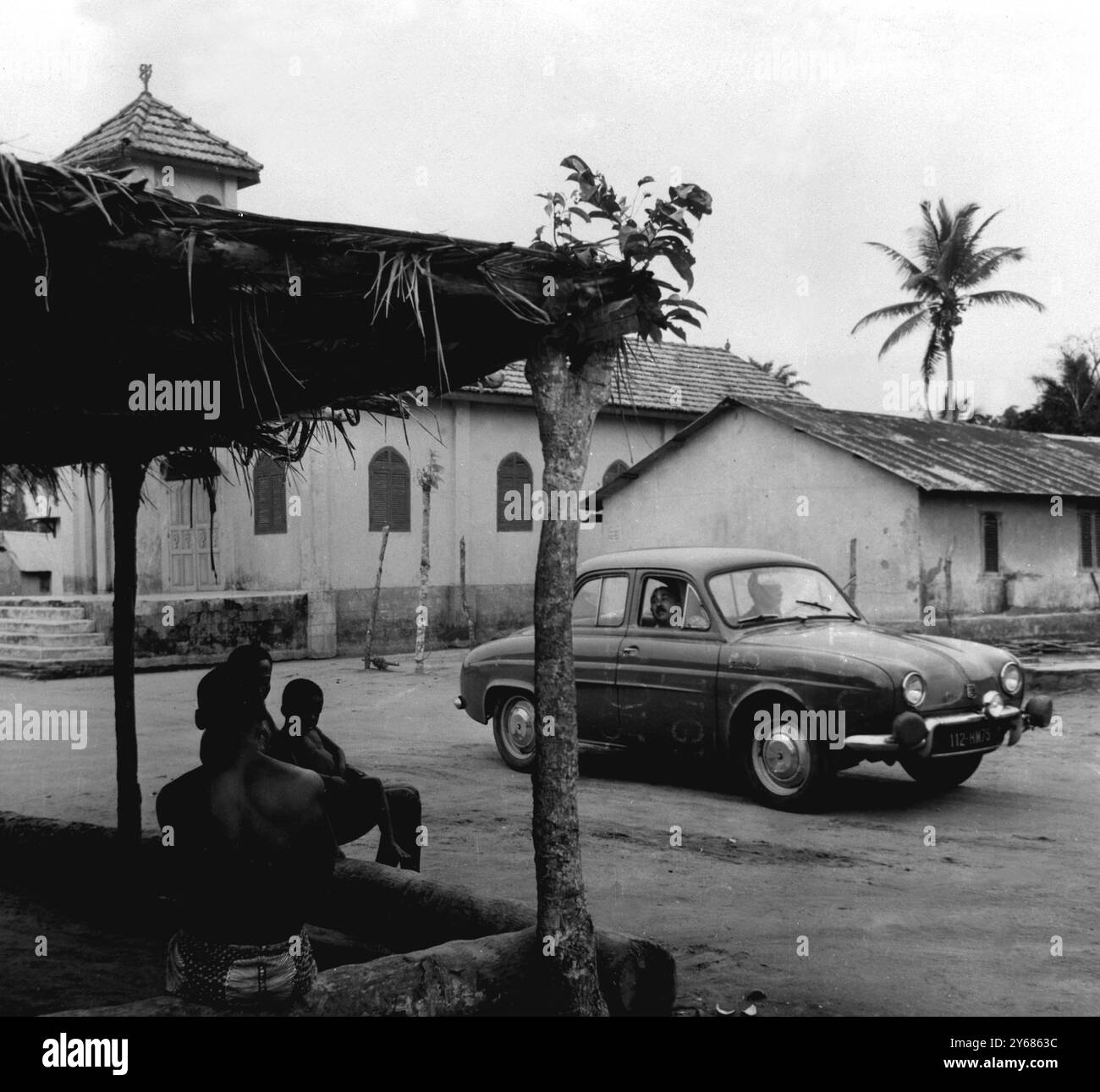 Percorso di rally attraverso villaggi nativi. Costa d'Avorio, Africa occidentale. Mentre i nativi guardano, una vettura Renault Dauphine passa attraverso il villaggio di Banco, vicino Abidjan, durante le prove per il 5° Rally della Costa d'Avorio, organizzato dall'Automobile Club della Costa d'Avorio. Il rally è partito da Abidjan ieri, e dopo aver percorso una distanza di circa 1.488 km i concorrenti torneranno oggi ad Abidjan per il traguardo. 22 febbraio 1959. Foto Stock