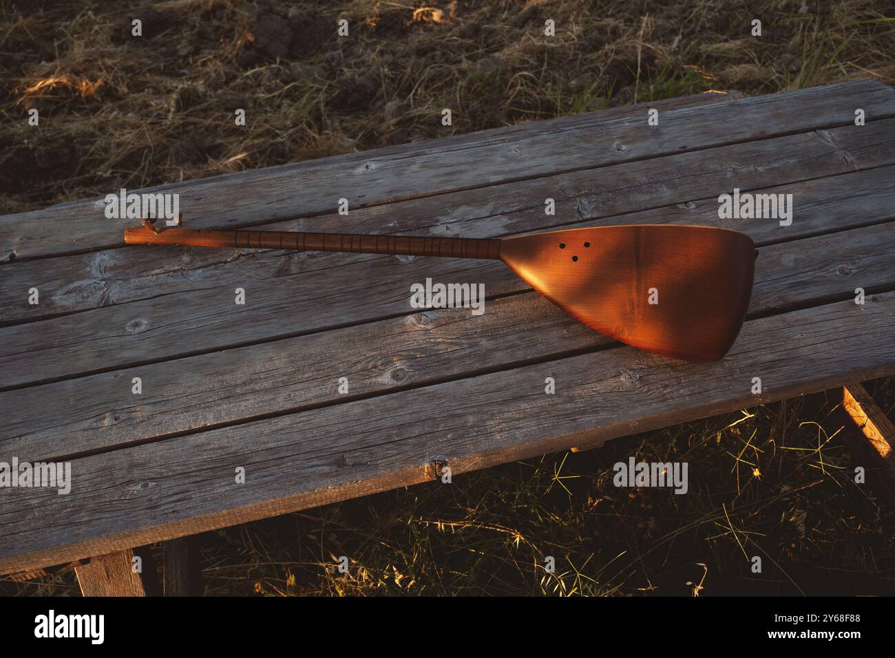 Un kopuz di legno splendidamente lavorato poggia su un tavolo di legno rustico al tramonto, catturando l'atmosfera tranquilla dell'uliveto Foto Stock
