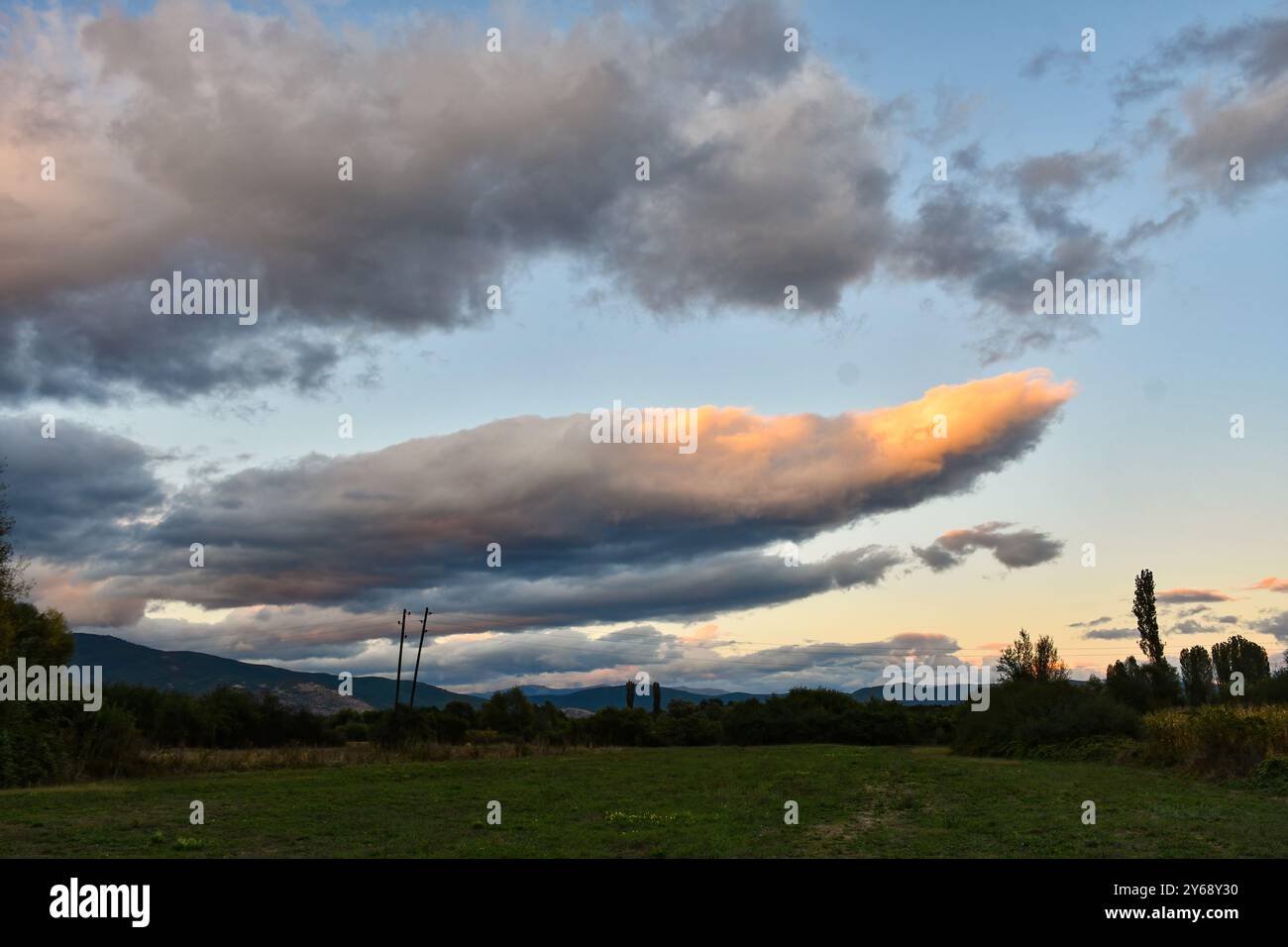 Un cielo pieno di belle nuvole, illuminato dal sole che tramonta dietro la montagna. Prima pioveva. Foto Stock