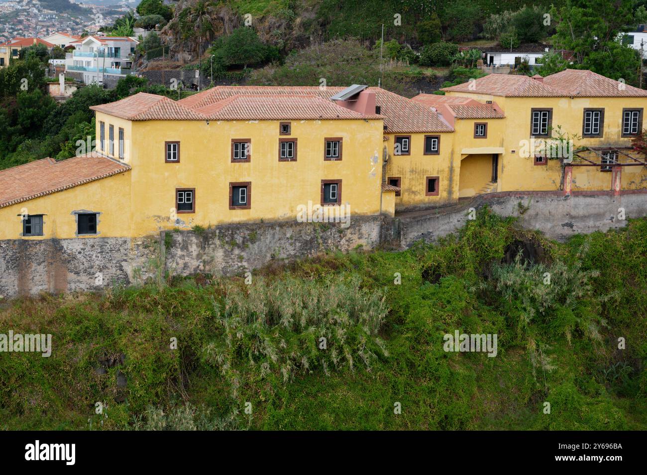 Affascinante edificio giallo arroccato su una collina a Madeira, architettura tradizionale in mezzo a lussureggiante vegetazione Foto Stock