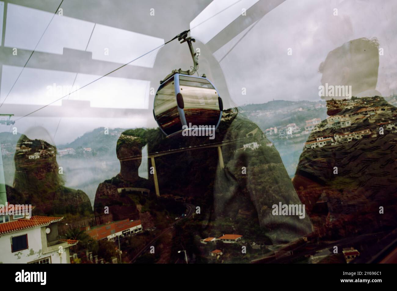 I riflessi dei passeggeri si fondono con la vista della funivia e delle montagne, creando una miscela surreale di movimento e paesaggio a Funchal Foto Stock