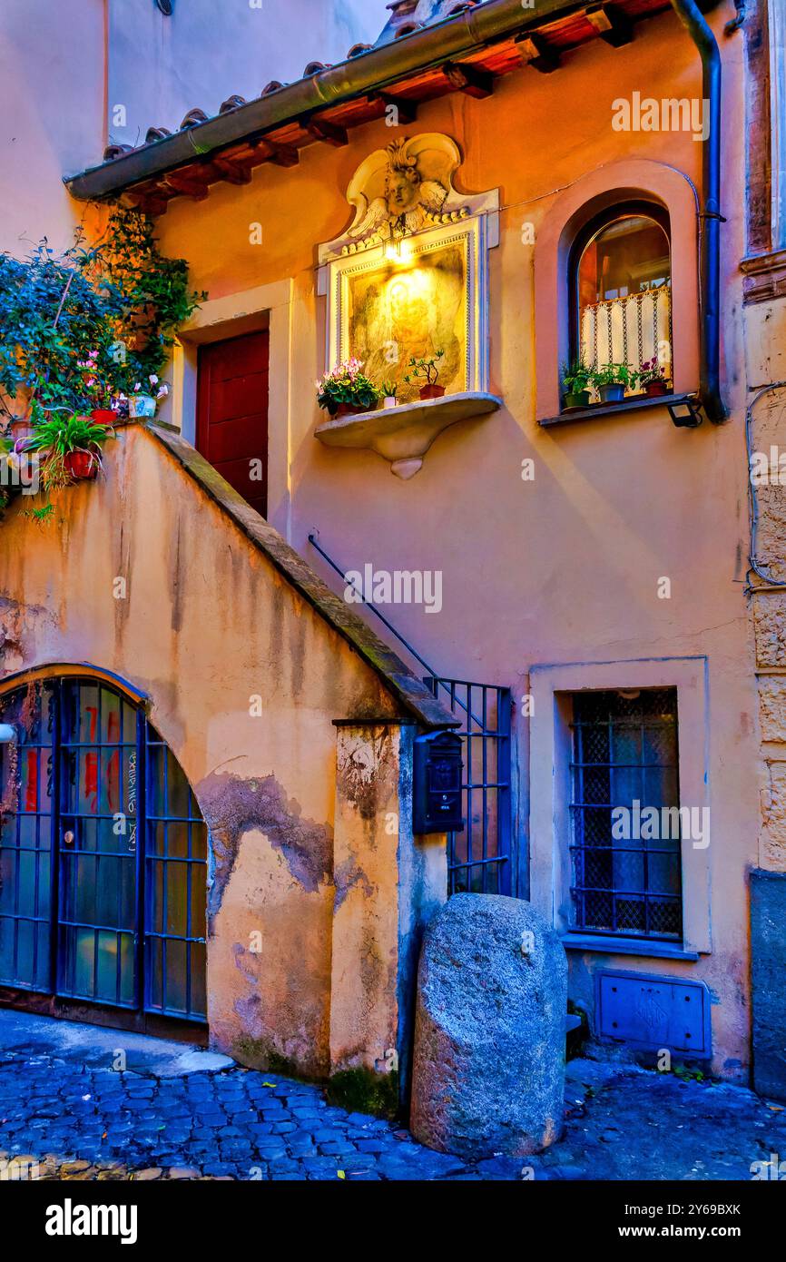Vista notturna di un'affascinante casa in via dell'Arco di San Calisto, Trastevere, Roma, conosciuta come la casa più piccola del quartiere, caratterizzata da un sacro Foto Stock