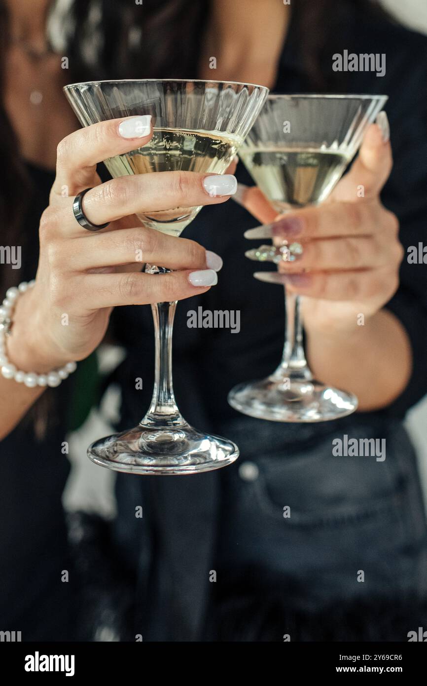 Due persone elegantemente vestite sorseggiano bevande frizzanti, alzando i bicchieri in un brindisi per celebrare un'occasione gioiosa, circondate da un'atmosfera chic Foto Stock