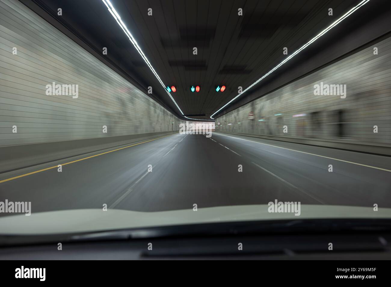 All'interno di un moderno tunnel veicolare, strade pavimentate con corsie segnalate, pareti orizzontali, luci continue in alto Foto Stock