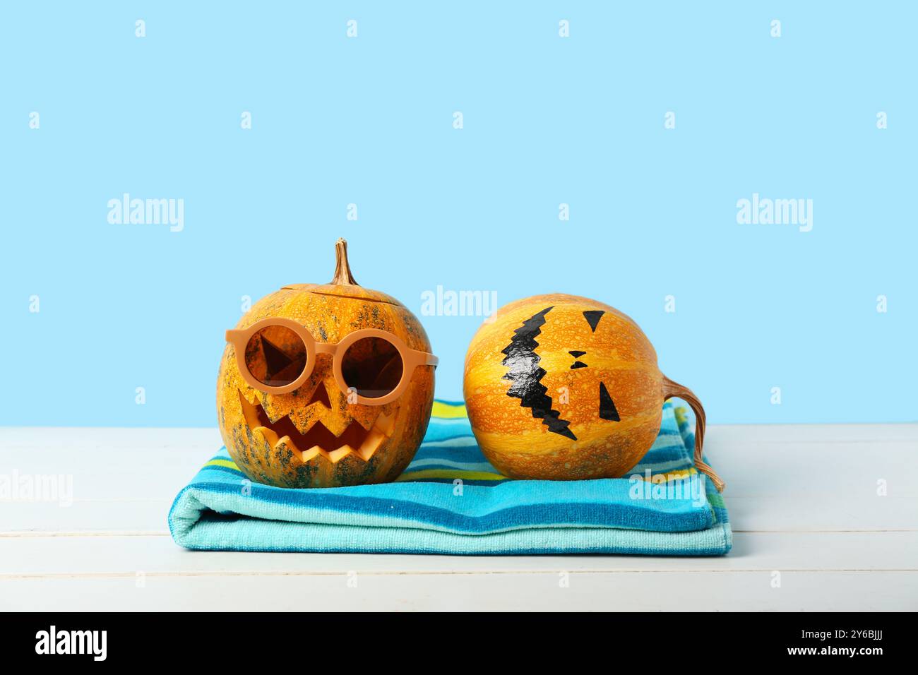 Zucche di Halloween con occhiali da sole e asciugamano su sfondo blu Foto Stock