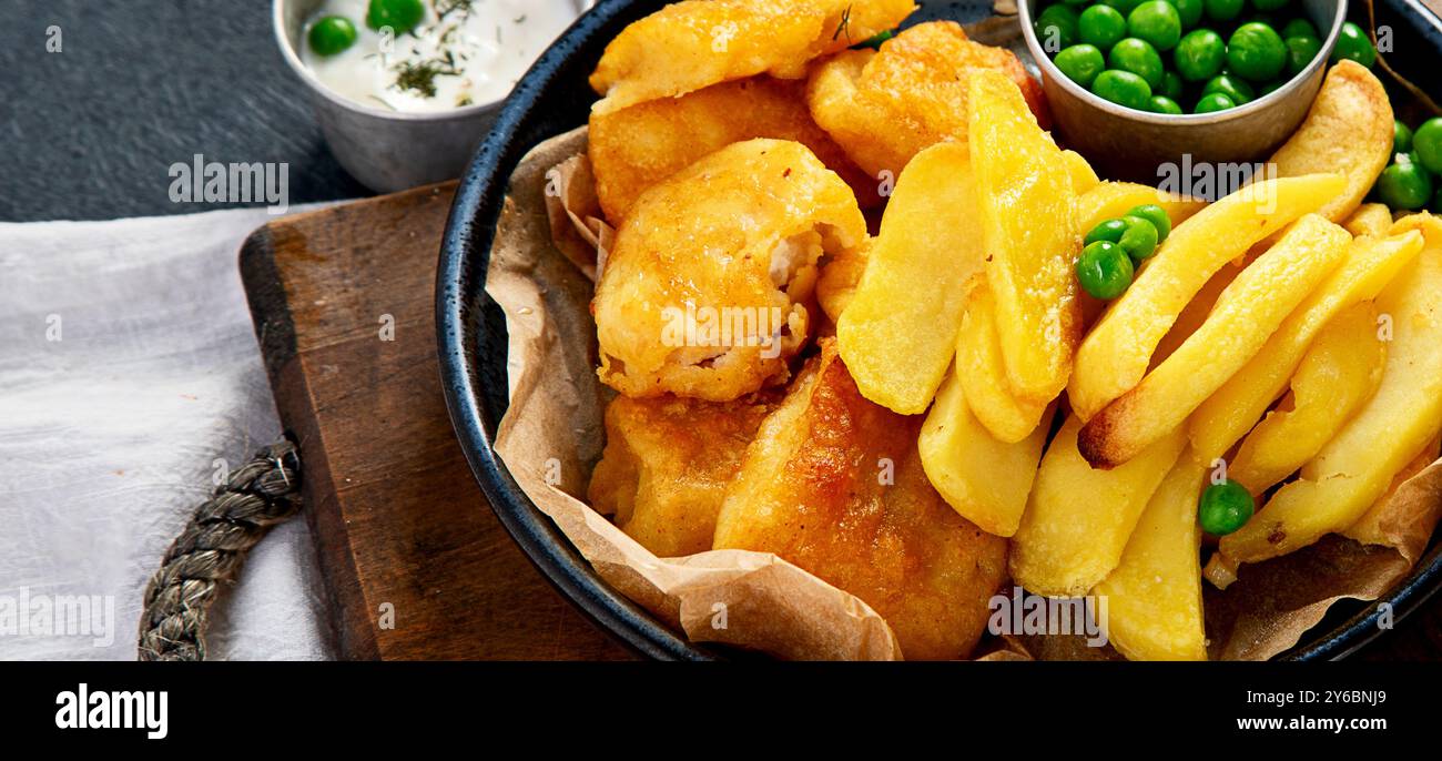 Piatto con pesce tradizionale britannico e patatine fritte su sfondo scuro Foto Stock