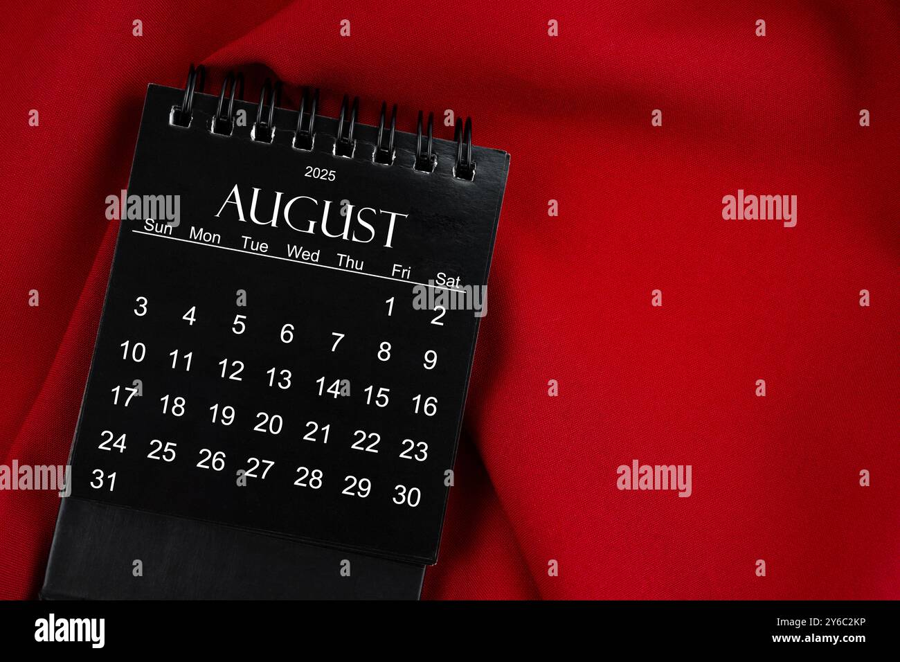 Agosto 2025 calendario desktop a spirale nero su sfondo tessile rosso. Foto Stock
