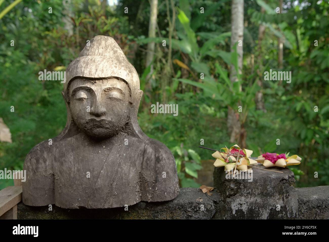Offerta spirituale Balinese accanto ad una scultura in legno nel villaggio artigianale di Pakudwi, Gianyar, Bali, Indonesia. Foto Stock