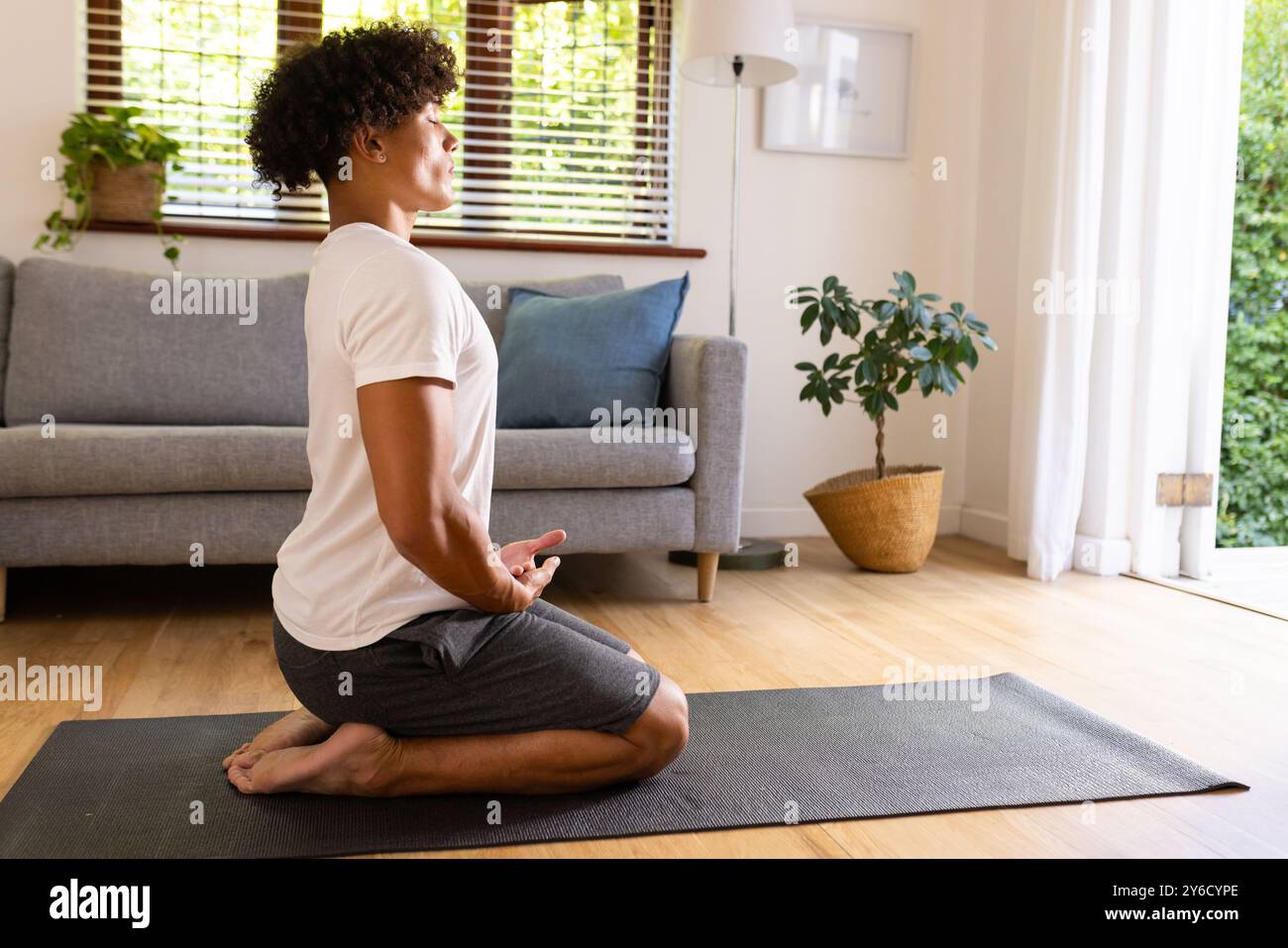 A casa, praticando yoga, uomo seduto sul tappetino in salotto, concentrandosi sulla respirazione Foto Stock