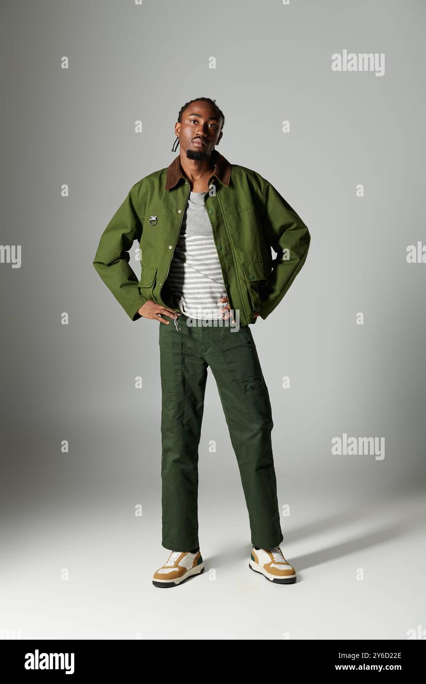 Un giovane uomo mostra il suo senso unico della moda con un abbigliamento verde mentre si trova su uno sfondo grigio Foto stock Alamy